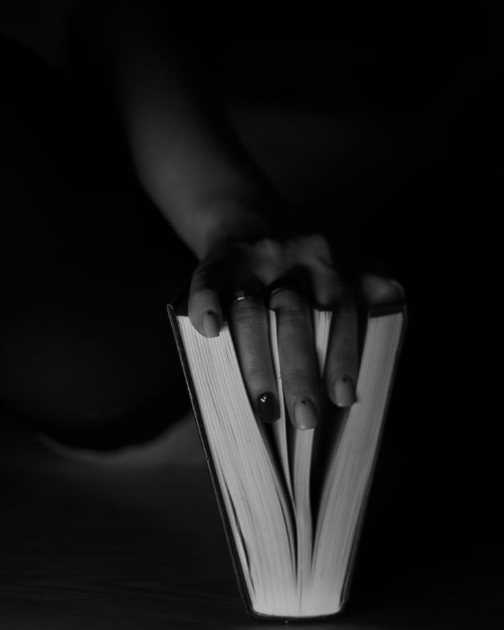 A hand slipped between the pages of a book standing open in low light